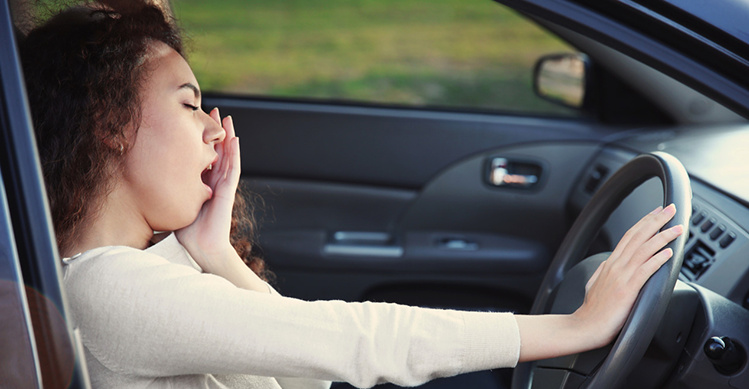 Curly haired girl sitting in the drivers seat and yawning.