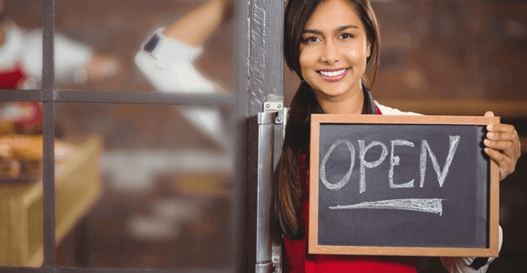 Woman holding a chalkboard sign with the word open written on it.