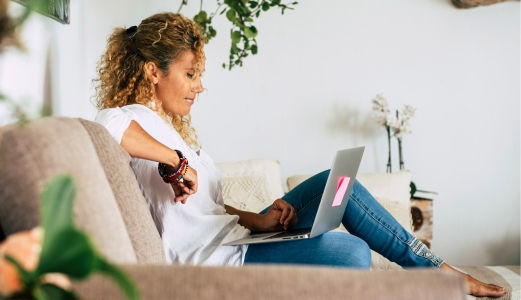 Curly haired woman relaxing on the couch using her laptop.