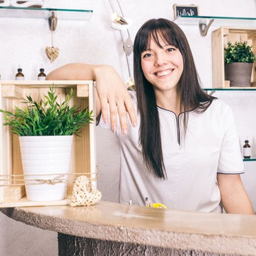 A worker smiling and leaning against a wooden box that has a pot plant in it.