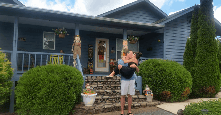 Couple kissing in front of their blue house.