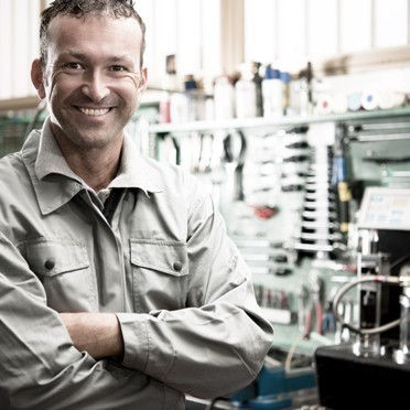 A mechanic smiling in their workshop with their arms crossed.