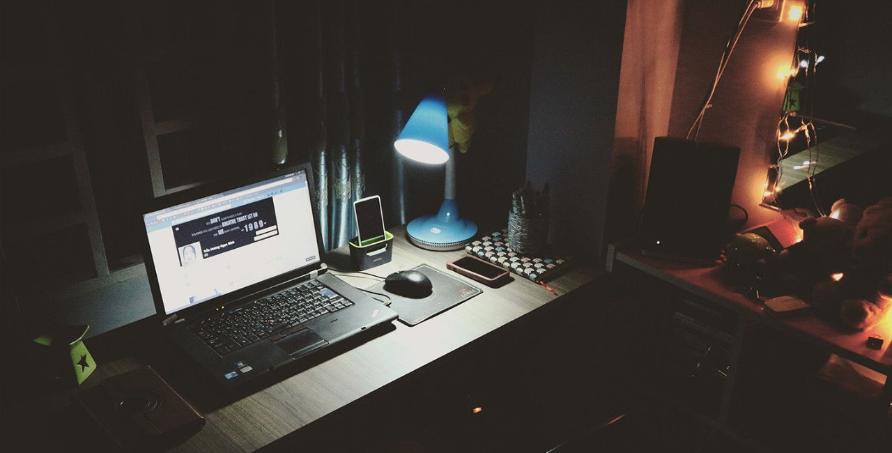 At home corner workstation with an open laptop and mouse, speaker and 2 phones on a desk