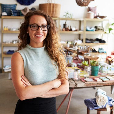 A retail staff worker standing inside their store smiling with their arms crossed.