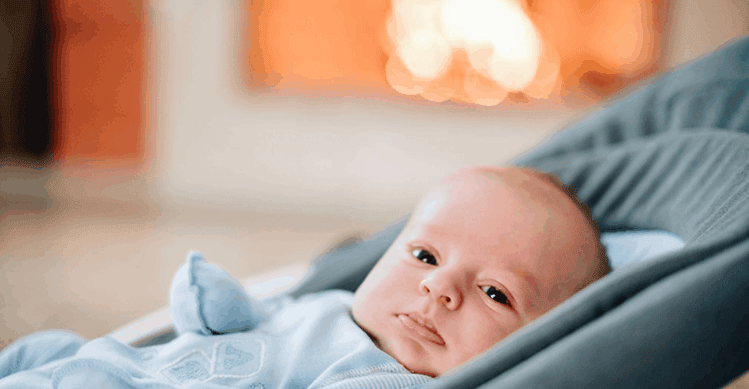 Baby wearing a blue jumpsuit lying down in a rocker.