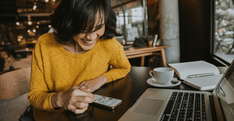 Woman wearing yellow jumper checking social media in a café.