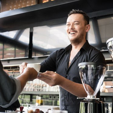 A barista wearing a black shirt serving a cup of coffee to a customer.