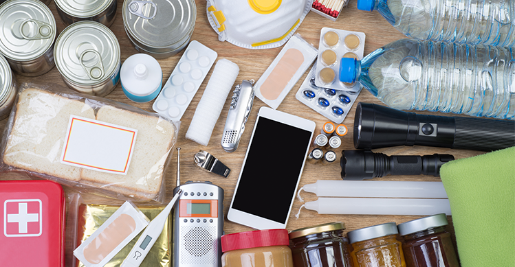 A collection of different items such as cans, jars, first aid kit, torches, water for an emergency it.